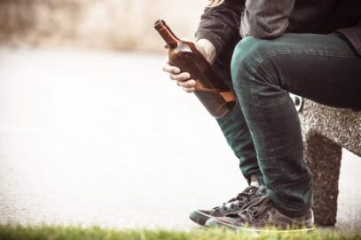 siedzący mężczyzna trzymający w dłoni butelkę z alkoholem